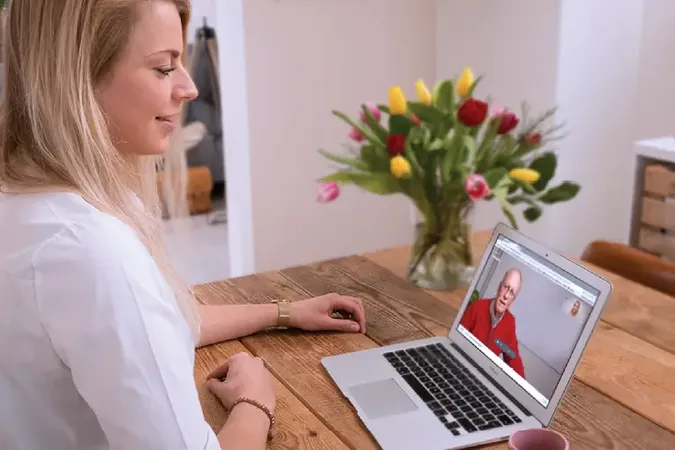 Vrouw achter de computer beeldbelt via WeSeeDo aan de keukentafel.