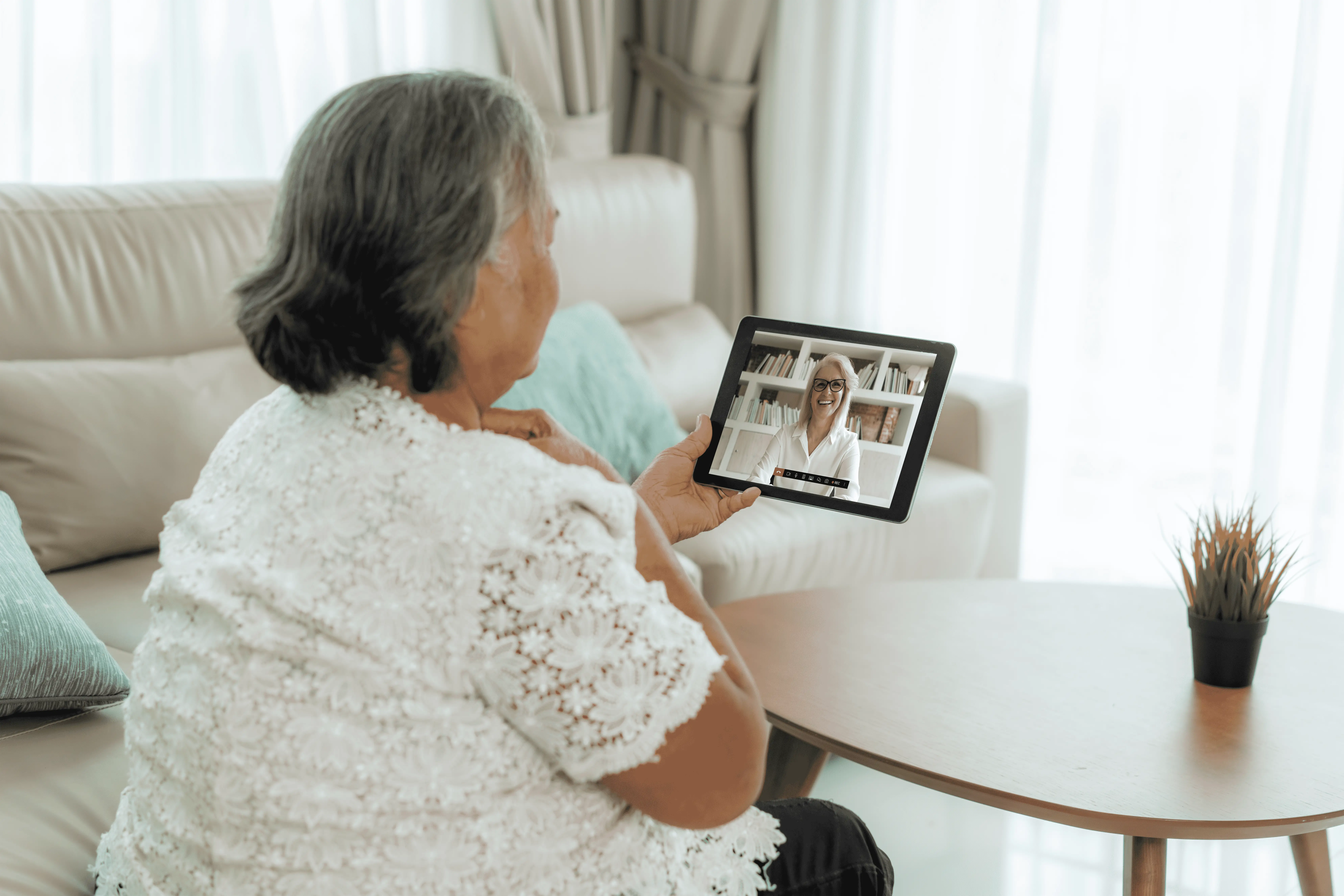 Oudere vrouw is thuis aan het beeldbellen met huisarts op Ipad
